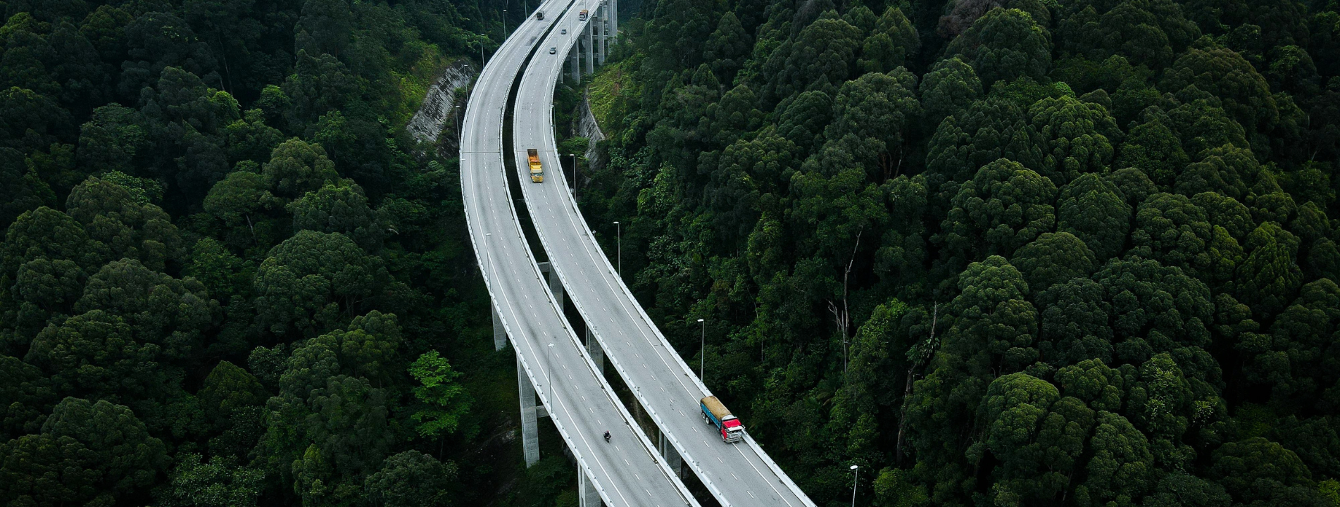 Aerial view of highway bridge through green forest with freight trucks
